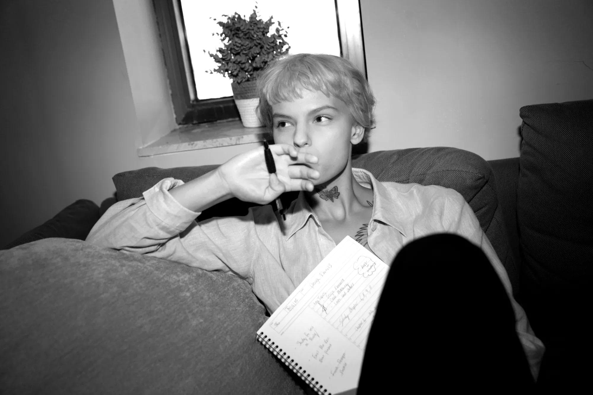 Person deep in thought, holding a pen to their mouth while going through notes on a sofa, reflective of the studious environment in Paris.