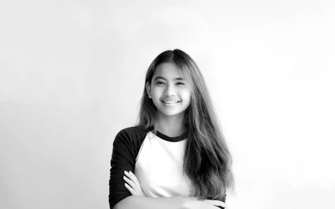 Cheerful young female UX student in Singapore with long hair and casual attire, arms crossed, embodying the connection and networking potential in professional courses.