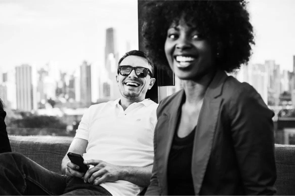 A business woman and man sitting down and smiling in front of a blurry city skyline represent the tech talent hiring offered by GA.