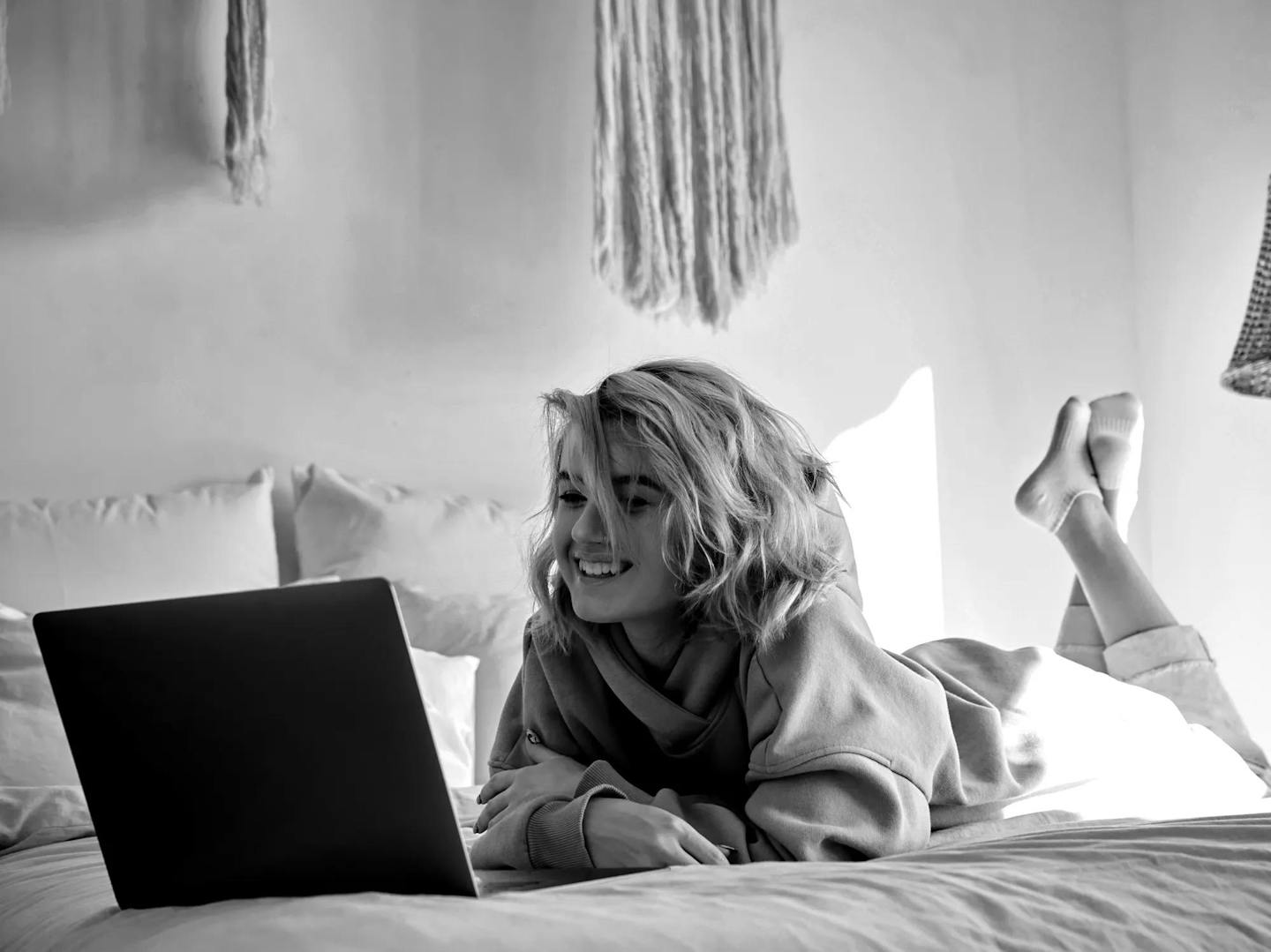 Happy hipster gen z teen girl with pink hair wear hoodie watching tv movie on laptop lying in bed. Smiling teenager make video conference call online, learning online video course, relaxing in bedroom