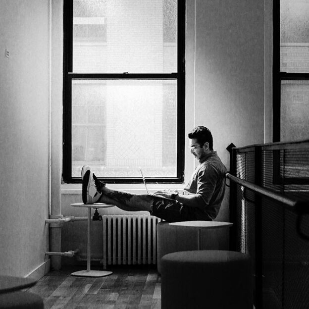 student sitting with legs up in front of a window in GA NYC campus looking at a laptop
